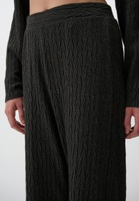 Zwarte gestructureerde wijde broek met een zigzagpatroon, voorzien van een hoge tailleband, zachte stof en een losse pasvorm, tentoongesteld tegen een effen achtergrond.