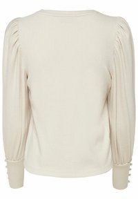 Kremowa bluzka z bufiastymi rękawami, prążkowaną teksturą i guzikami na mankietach. Prosty okrągły dekolt podkreśla jej design.