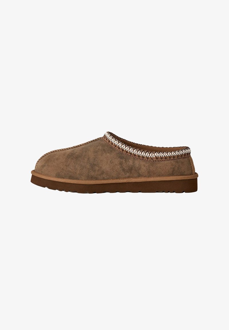 Zapato marrón de ante tipo slip-on con punta redonda, parte superior texturizada y un acento trenzado alrededor del cuello. Presenta una suela de goma plana.