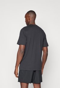 Camiseta negra de manga corta hecha de tejido suave, con cuello redondo y corte relajado, acompañada de pantalones cortos negros. Diseño simple, sin patrones.