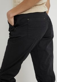 Svarta cargobyxor i bomull med flera fickor, med en avslappnad passform och textilstruktur. Inkluderar synlig sömnad och metallaccenter.