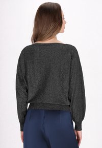 Schwarzer, glitzernder, kurz geschnittener Pullover mit weitem Bootsausschnitt, langen Puffärmeln und geripptem Saum. Getragen mit blauen Satin-Hosen.