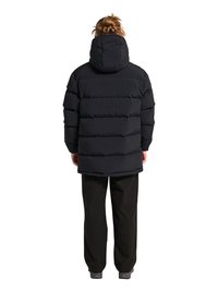 Person med en topknude-frisure iført en sort hætte-pufferjakke, sorte bukser og grå sko, stående med ryggen mod betragteren.