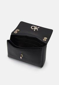 Černá kožená kabelka se strukturovaným tvarem, zlatými kovovými doplňky a vyraženým logem CK. Otevřený vnitřek s hlavním oddělením a kapsami.