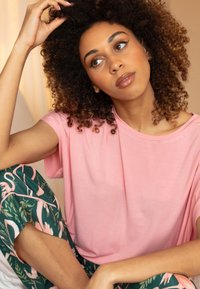 Jasnoróżowa koszulka z krótkim rękawem w połączeniu z zielonymi spodniami z motywem różowego flaminga. Miękka tkanina o luźnym kroju.