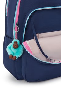 Sac à dos bleu marine avec des fermetures éclair roses et turquoise. Présente un porte-clés en peluche de singe bleu clair attaché à une fermeture éclair.