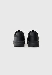 Black sneakers with smooth leather upper, padded collar, and textured rubber soles. Rear pull tab for easy wear.