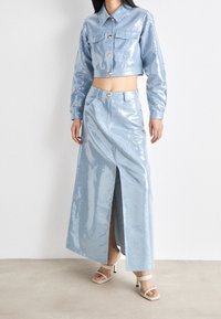 Ljusblå, glänsande kort jacka med två framfickor och guldknappar, kombinerad med en matchande lång kjol med hög slits. Slät textur.