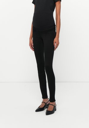 Black skinny jeans with a smooth texture, mid-rise waist, adjustable panel for comfort, and paired with black pointed-toe slingback heels.
