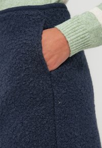 Falda texturizada azul marino con un material suave y difuso y un bolsillo lateral. El borde presenta un ribete oscuro en contraste que aporta un detalle estructural.