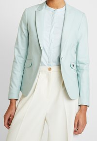 Ljust blå skräddarsydd kavaj i slät tyg, med en enkel knäppning, två framfickor och en snibbkrage.