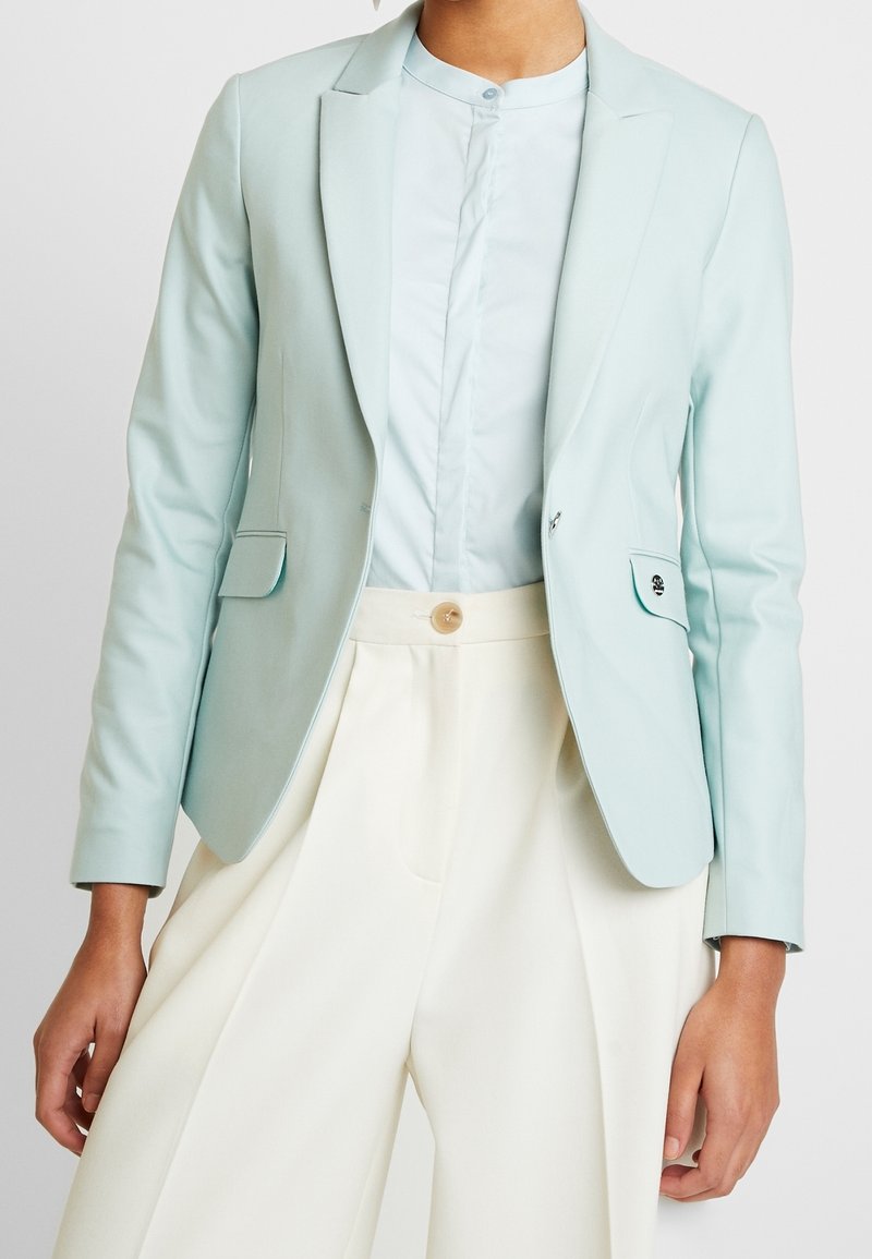 Ljust blå skräddarsydd kavaj i slät tyg, med en enkel knäppning, två framfickor och en snibbkrage.