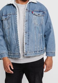 Blekt blå denimjacka med vit fleecekrage, framfickor och tryckknappar. Använd över en grå sweatshirt med rund halsringning.