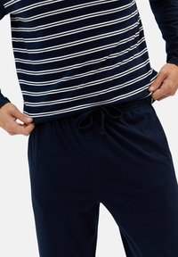 Ensemble de pyjama marine comprenant un haut à rayures à manches longues avec des rayures blanches et un pantalon à taille élastique assorti. Tissu doux avec une texture lisse.