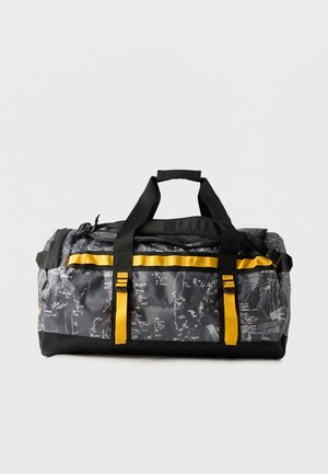 Borsone grigio e nero con motivi astratti bianchi e cinghie e fibbie giallo brillante, su uno sfondo chiaro e uniforme.