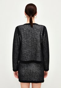 Maglione a maglia bianco e nero con motivo testurizzato, scollatura rotonda e maniche lunghe. La vestibilità è leggermente ampia con lunghezza cropped.