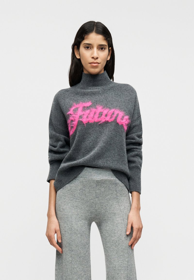 Γκρι πουλόβερ ζιβάγκο με χνουδωτό ροζ γράφημα "Μέλλον" στο στήθος· συνδυασμένο με ανοιχτό γκρι παντελόνι με φαρδιά πόδια.