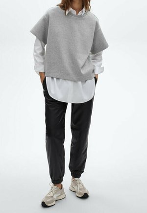 Grijze korte mouw sweatshirt over een wit blouse met knoopjes, gecombineerd met zwarte taps toelopende trainingsbroek en beige sneakers.