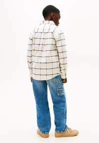 Hvid skovmandsskjorte med marineblå striber, knaplukning og lange ærmer. Sammen med blå jeans og beige slip-on sko.