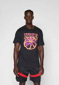 Sort bomuld t-shirt med et flerfarvet grafik af en basketball og ordet "NIKE" i fed skrift. Båret med sorte shorts med røde accenter.