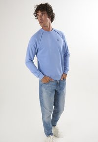 Felpa azzurra realizzata in tessuto morbido, con scollo a girocollo e maniche raglan. Abbinata a jeans azzurri e sneakers bianche.