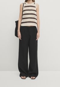 Top in crochet a righe crema e marrone scuro, abbinato a pantaloni larghi neri e una borsa intrecciata nera.