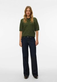 Zielony sweter o fakturowanym splocie z krótkimi rękawami, zestawiony z ciemnoniebieskimi jeansami o szerokich nogawkach. Strój charakteryzuje się klasycznym, casualowym stylem.