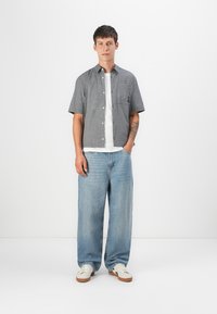 Short-sleeve, black and white checkered shirt, accompanied by a white t-shirt and light blue wide-leg jeans, worn with white sneakers.