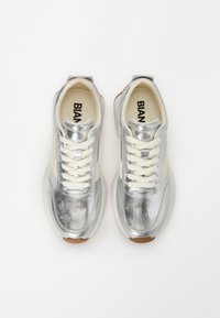 Silberne Sneakers mit metallic Finish, weißen Akzenten und beigen Schnürsenkeln. Eigenschaften sind eine abgerundete Schuhspitze und eine strukturierten Gummisohle.