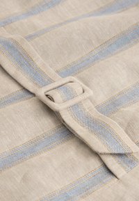 Béžová látka s modrými a krémovými pruhmi, vybavená preloženým remienkom a obdĺžnikovou prackou. Textúra pôsobí tkaná a hladká.