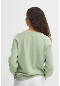Hellgrüner Pullover mit lässiger Passform, geripptem Saum und Raglanärmeln. Weiche Textur und schlichtes Design mit minimalen Details.