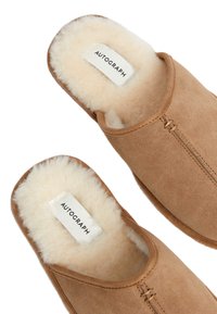 Pantofole marroni in suede con fodera interna in morbida pelliccia in crema. Presentano cuciture minime e un'etichetta che recita "AUTOGRAPH."