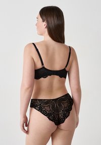Schwarzer Spitzen-BH und passende Panties mit floralem Muster und gewellten Kanten. Verstellbare Träger und Häkchenverschluss auf der Rückseite.