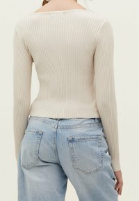 Haut beige côtelé à manches longues avec une silhouette ajustée, associé à un jean taille haute bleu clair avec poches arrière et une légère déchirure.