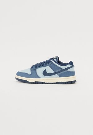 Baskets basses Nike en bleu clair et bleu foncé avec une semelle blanche et des lacets bleu foncé, vues de profil sur fond blanc.