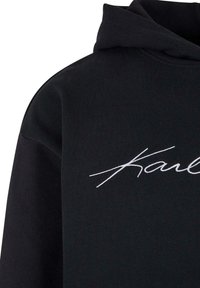 Sudadera negra con una textura suave que presenta texto bordado en blanco. El diseño incluye una capucha con cordones y un ajuste relajado.