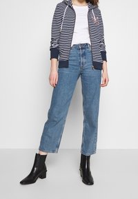 Felpa con zip a righe blu navy e bianche, con cappuccio con cordino, abbinata a jeans dritti a vita alta blu chiaro e stivali neri alla caviglia.