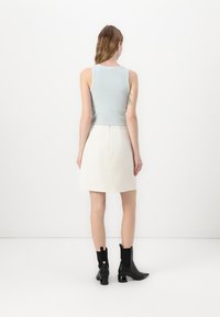 Haut sans manches bleu clair au design ajusté, associé à une mini-jupe blanche texturée. Bottines noires avec un talon bloc.