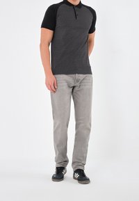 Polo shirt noir et blanc à manches courtes avec un motif géométrique, associé à un jean gris clair et des baskets noires avec des accents bleus.