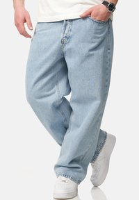 Light blue denim jeans, relaxed fit, featuring classic five-pocket design. Finished with a cuffed hem and paired with white sneakers.