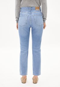 Ljusblå denimjeans med en avsmalnande passform, med två bakfickor och en brun etikett vid midjan. Slät textur, avslappnad design.