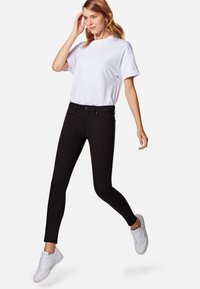 Jeans skinnies negros combinados con una camiseta blanca y zapatillas blancas. Los jeans tienen un diseño ajustado y un estilo clásico de cinco bolsillos.