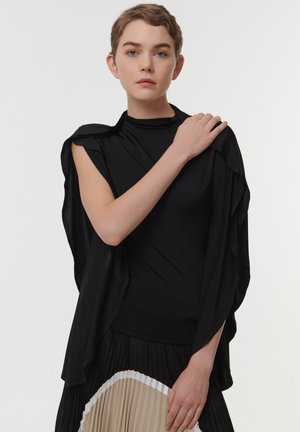 Zwarte, gelaagde top met hoge hals en gedrapeerde mouwen, gecombineerd met een geplooide zwarte en beige rok. Soepele stof met een vloeiende silhouet.