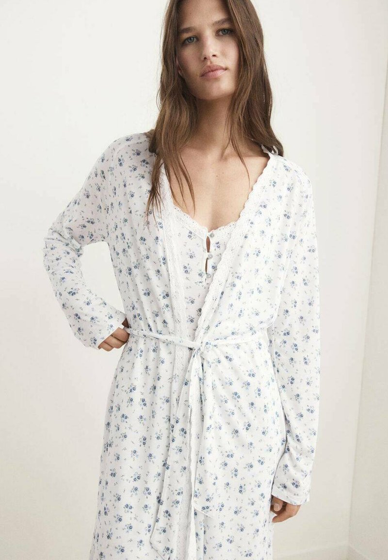Robe blanche à motifs floraux bleus, manches longues et dentelle en finition. Entièrement nouée à la taille avec une ceinture assortie pour une silhouette définie.