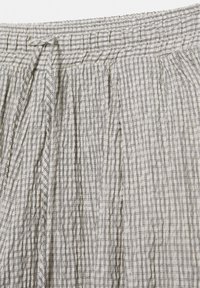 Elastischer Bund mit gebundener Kordel an weißem Stoff mit kleinem schwarzem Karomuster und vertikalen Falten.