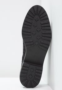 Semelle de chaussure en caoutchouc noir avec un motif de bande de roulement texturé, présentant des rainures et des accents en forme de croix pour l'adhérence et la stabilité.