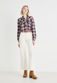 Blusa de cuadros en negro y rojo con detalle de lazo, combinada con pantalones de tiro alto de pierna ancha blancos y botas de tobillo de tacón marrones.