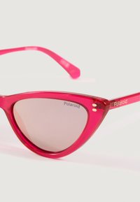 Svijetlo ružičaste mačkaste sunčane naočale s lagano obojenim staklima, s Polaroid logotipom na staklu i sljepoočnicama.