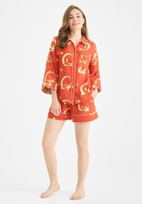 Röd pyjamas uppsättning med kort ärm bestående av en skjorta med knäppning och shorts med ett mönster av månar och stjärnor i beige. Tillverkad av bomull, avslappnad passform.