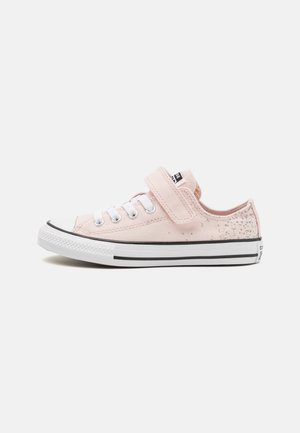 Zapatilla de lona rosa con cordones blancos y una correa de Velcro. Presenta una puntera de goma y líneas de acento negras en la suela.